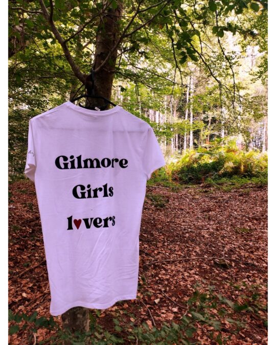 T-shirt bianca vista da dietro appesa nel bosco con scritta nera Gilmore Girls lovers e cuore rosso