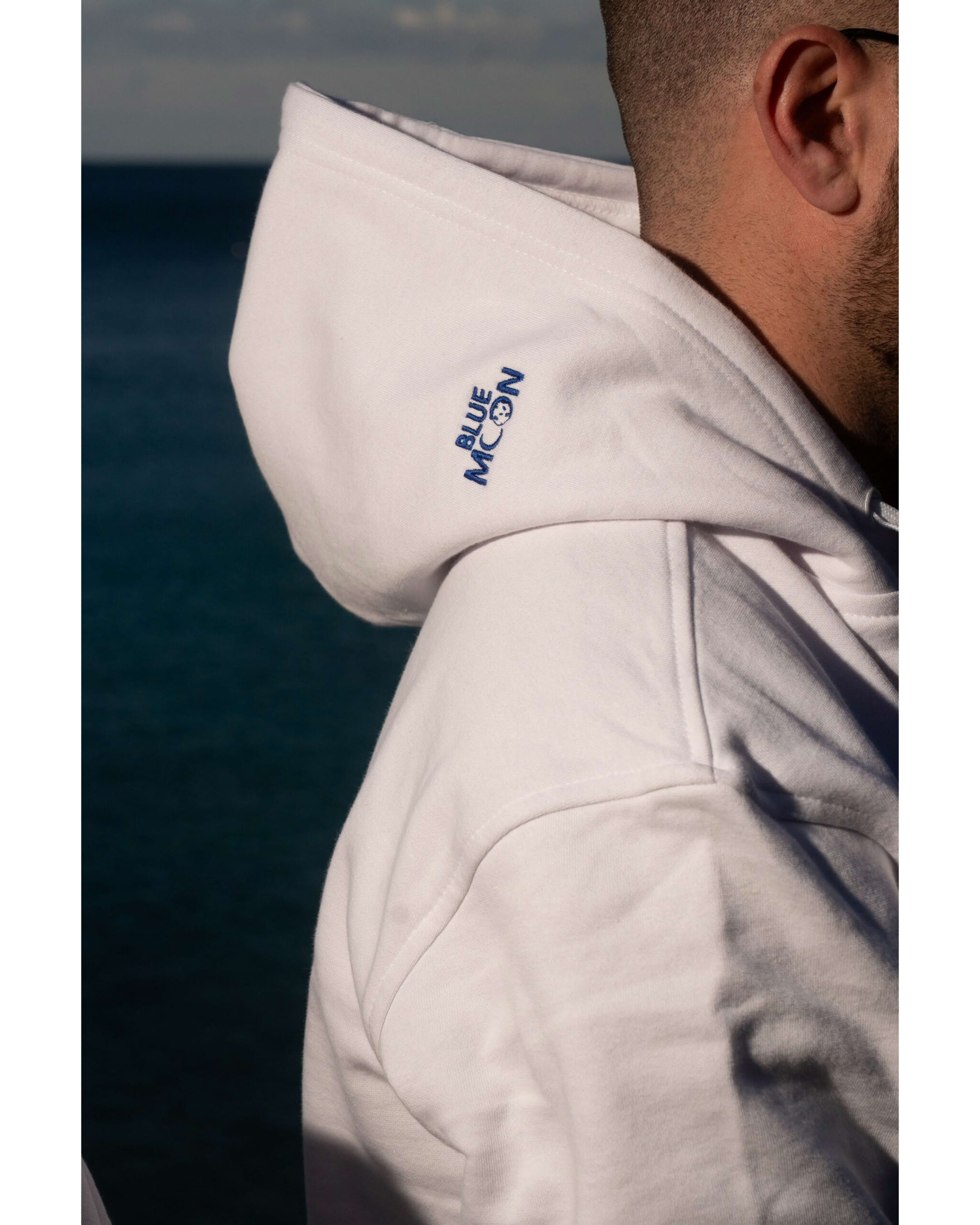 Profilo uomo con dettaglio cappuccio felpa bianca e scritta ricamata blu Blue Moon