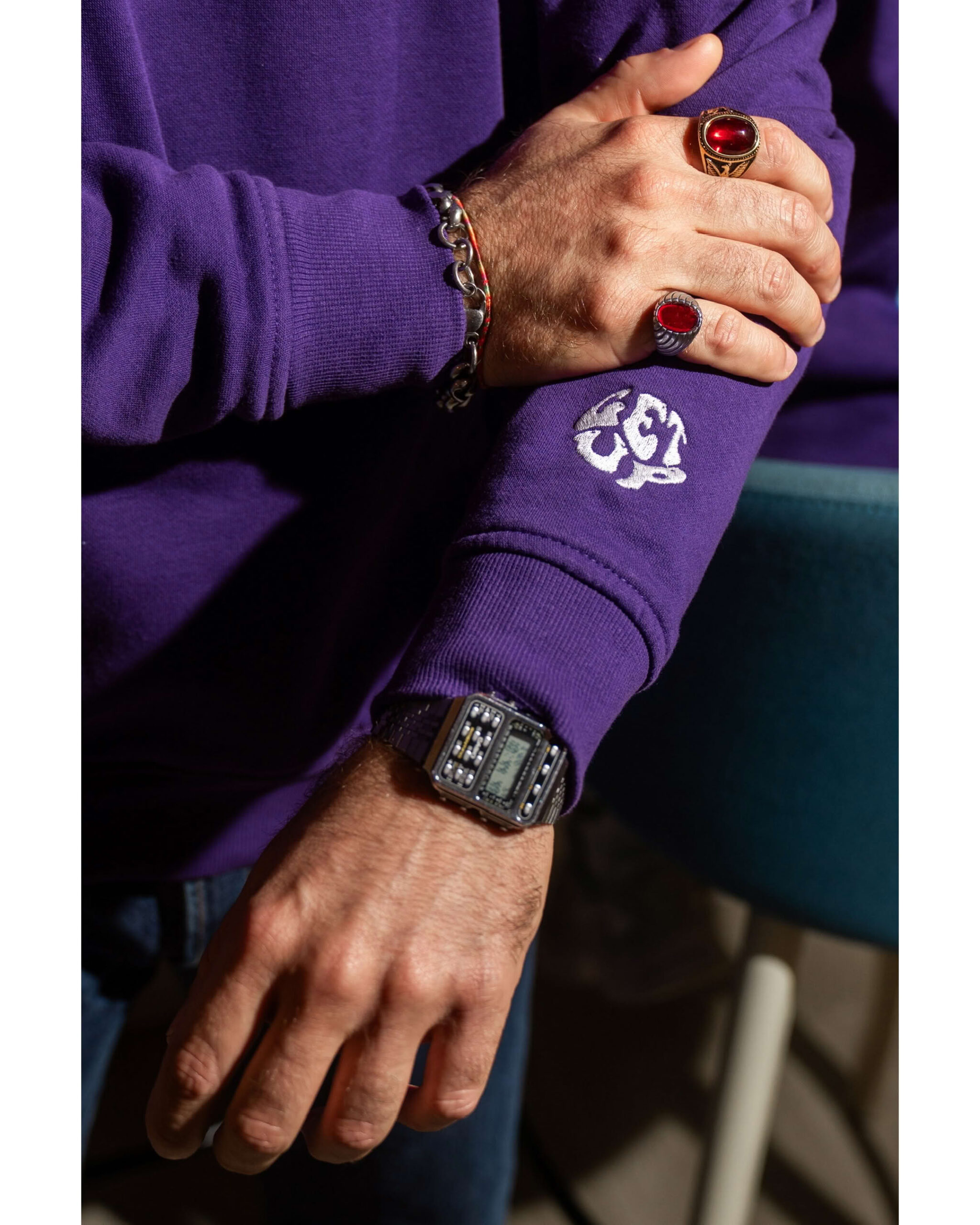 Dettaglio braccio uomo con orologio vintage, anelli e ricamo Get Up sul polsino della felpa viola.