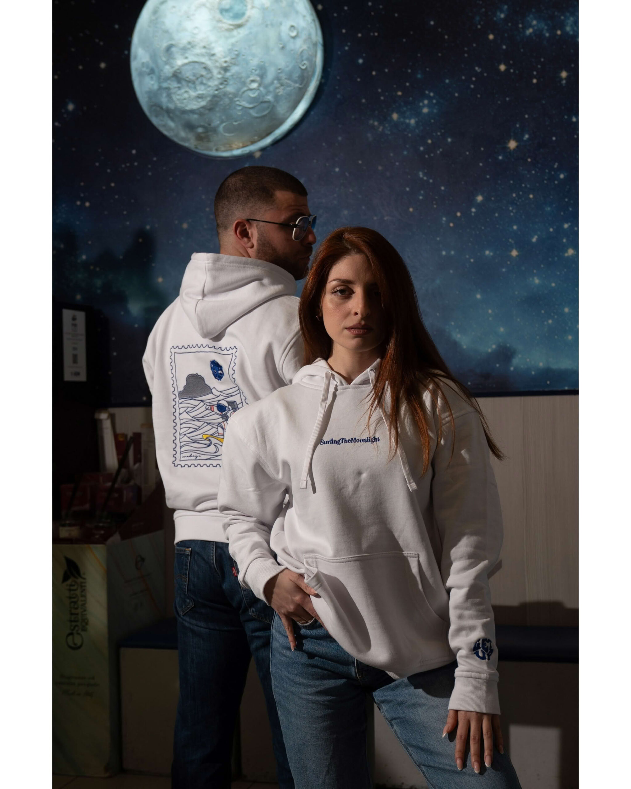 Coppia in studio: lui di spalle mostra grafica astronauta, lei di fronte con scritta SurfingTheMoonlight.