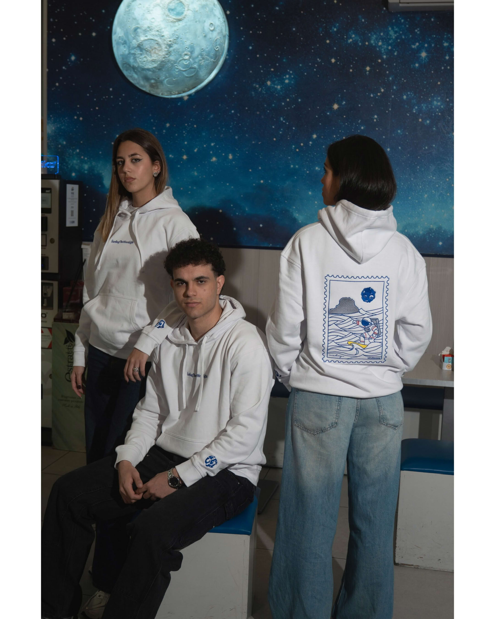 Tre modelli in posa studio con sfondo spaziale indossano felpe bianche coordinate fronte e retro.