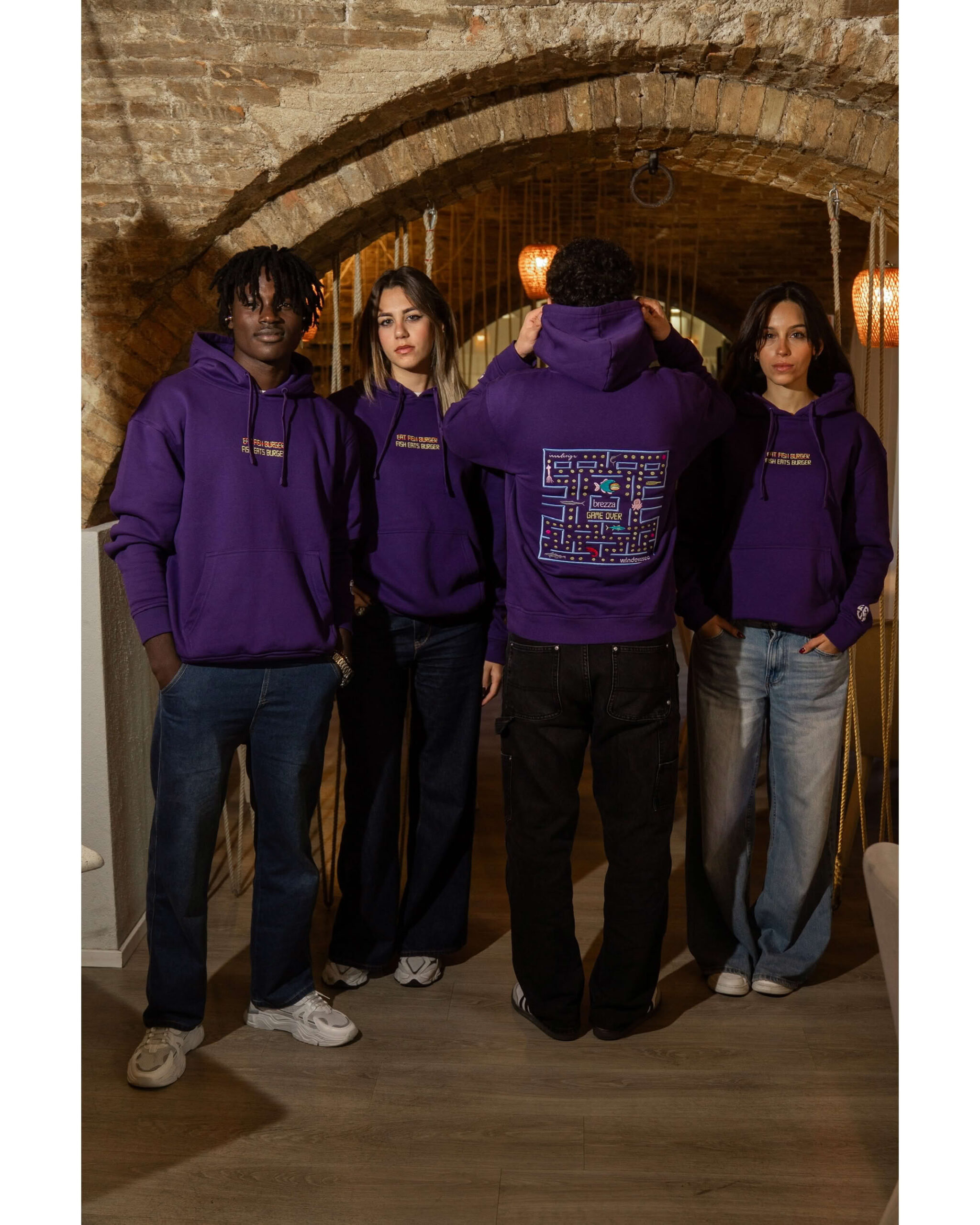 Gruppo di quattro ragazzi, uno di spalle mostra il maxi ricamo posteriore a labirinto stile Pacman con scritta Brezza Game Over.