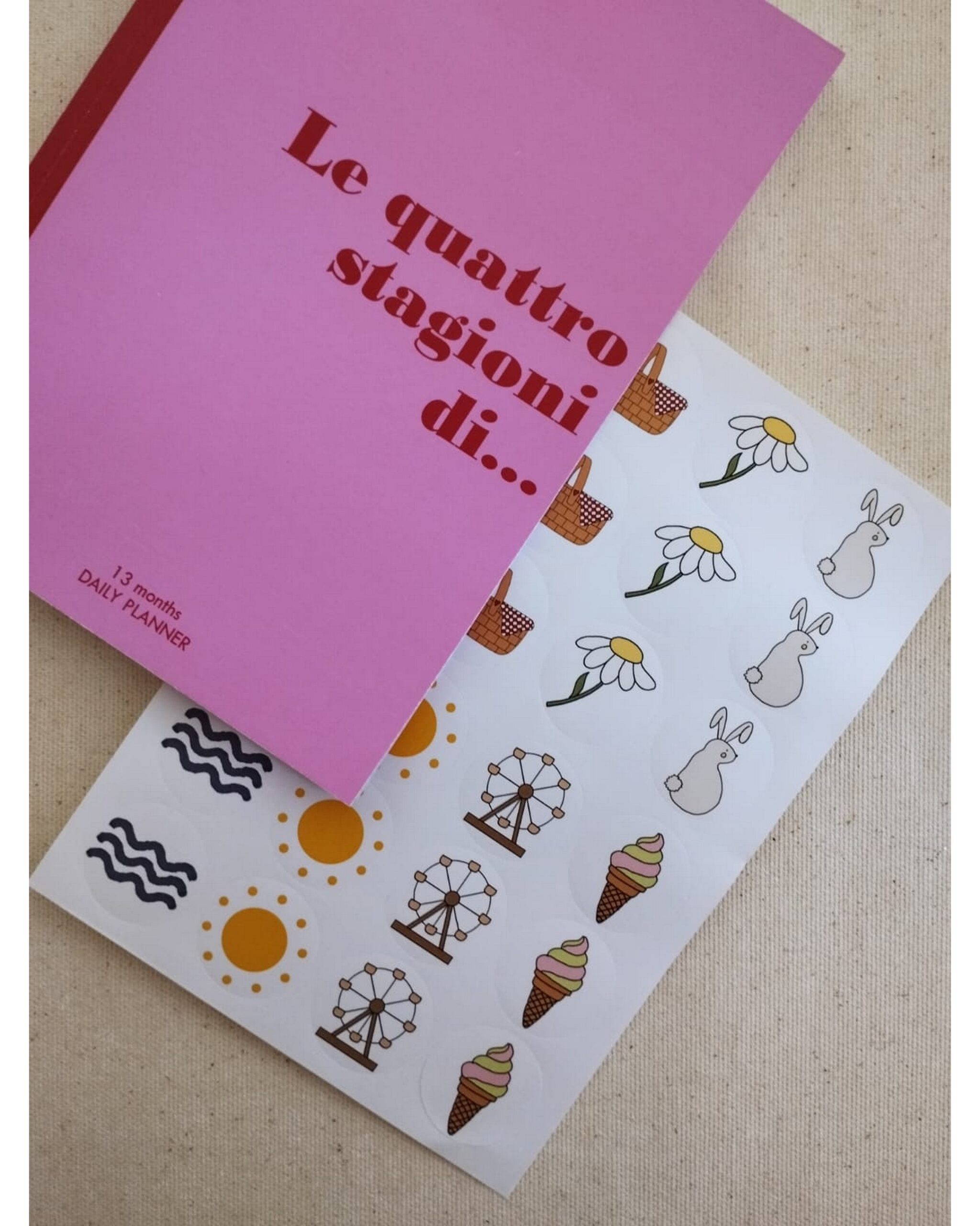 Planner aperto su pagina 'Estate' con onde gialle e pagina 'Primavera' con quadretti rosa che si solleva