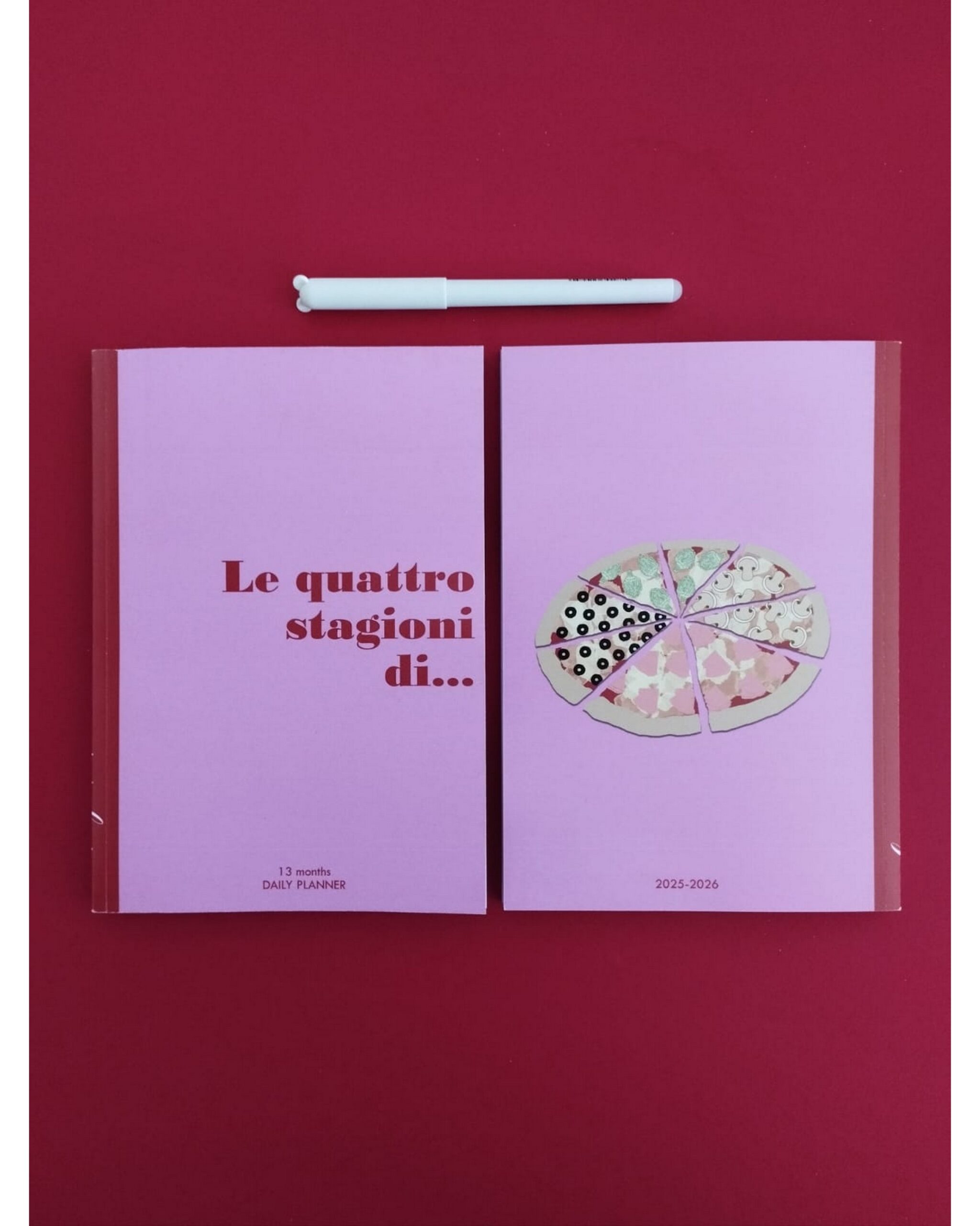 Un planner rosa con fronte e retro affiancati: uno con titolo e l'altro con illustrazione di una pizza a fette, penna bianca sopra
