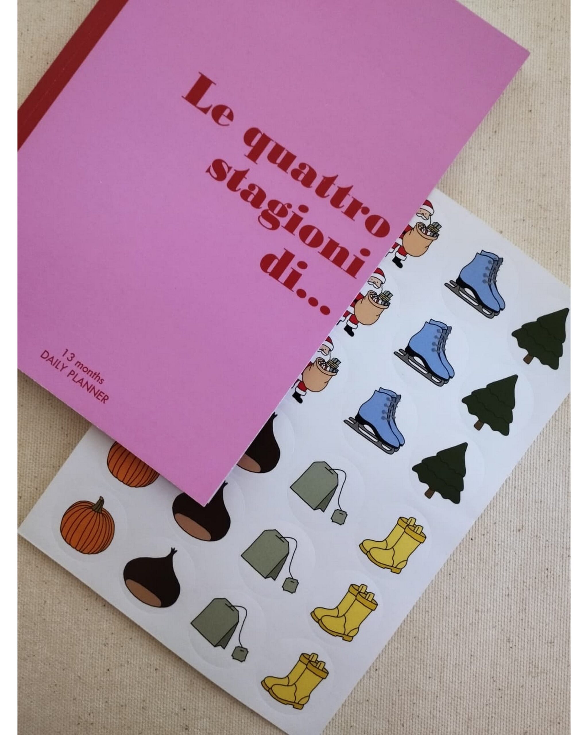 Planner rosa 'Le quattro stagioni di...' con foglio di sticker invernali e natalizi su fondo chiaro